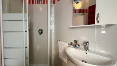 Bagno piccolo con doccia, lavabo e dettagli rossi sulle piastrelle