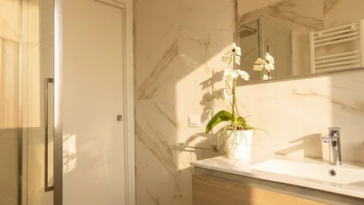 Bagno moderno con lavabo in legno e orchidea bianca su parete in marmo