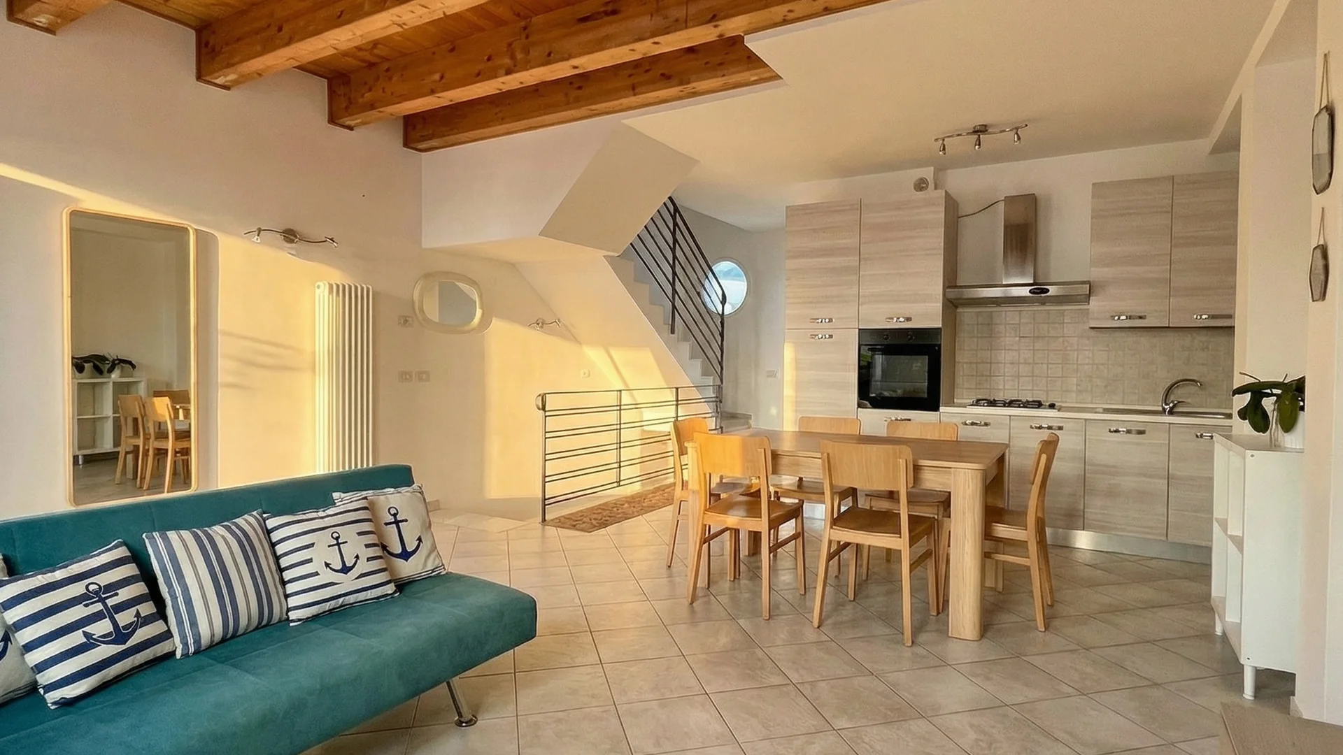 Soggiorno con divano verde, cucina moderna e tetto in legno a vista